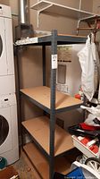 Full view of utility storage shelf with four wooden shelves, black metal frame, adjacent to laundry machines and water heater.