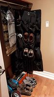Image of black fabric shoe storage bag hanging with multiple pairs of shoes inside some pockets and shoes lined on the floor in front.