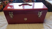 Closed red metal toolbox with black handle and silver latches, showing Beach brand decal on front.