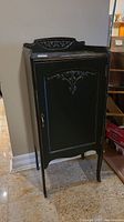 Full view angled photo of vintage wooden storage cabinet with carved details and metal latch on front door.