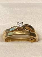 Front view of both rings stacked on white surface showing diamond solitaire and band profiles.