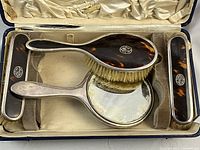 Interior of original satin-lined case showing hair brush, hand mirror and two clothes brushes