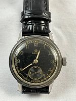 Front view of watch dial showing black face, gold numerals, hands, and subsidiary seconds dial