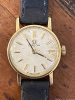 Front view of watch face showing off-white dial, applied gold baton markers, gold hands and Omega logo