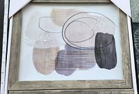 Abstract art print featuring soft neutral tones with overlapping oval shapes, linear and dotted details, framed in light wood.