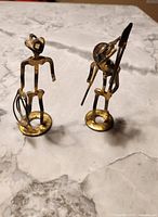 Two small metal sculptures on a marble surface, showing front view of cowboy and miner figures made from horseshoe nails.