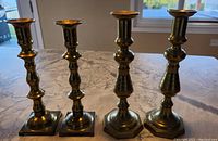 Four brass candlesticks grouped on marble surface showing overall size and design differences between two sets.