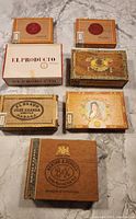 Seven vintage cigar and cigarette boxes arranged on floor showing various designs and brands.
