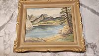 Framed landscape oil painting by A.L. Miller showing water, shore, trees and mountains.