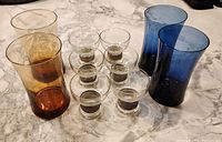 Top-down view of all 10 glassware pieces arranged on a marble countertop showing the shape and tint color differences for the blue and amber sets, plus the ring pattern on the aperitif glasses.