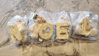Four white stuffed bears in sealed bags, each holding letters N, O, E, L