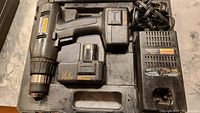 Cordless drill with attached battery, extra battery, and charger on a black plastic carrying case