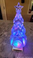 Illuminated Christmas tree figurine glowing blue with suspended sparkles inside, star on top.