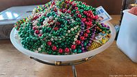 Wide view of frosted glass bowl on metal stand filled with colorful Mardi Gras bead necklaces