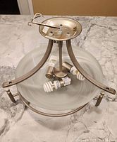 Top view of pendant chandelier showing the metal frame, central rod, and three included bulbs inside the frosted glass bowl.