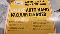Sears product box showing features and specifications of the Deluxe Auto Hand Vacuum Cleaner in French and English.