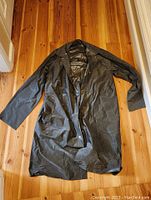 Front view of the black heavy duty raincoat laid flat on wooden floor, showing snap button closure and two front pockets