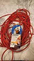Both extension cords shown: long orange cord and smaller blue NOMA cord in original packaging.