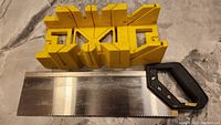 Yellow plastic miter box with saw laid inside on a marble surface.