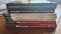 Stack of eight motorcycle performance and repair books showing titles and spines.