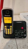 Close-up of Panasonic cordless handset in base showing 'Insert battery' on screen and phone base with control buttons and message display