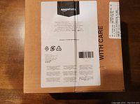 Top view of original sealed AmazonBasics packaging box on a wooden surface, showing multi-language product label and care instructions.