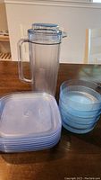Clear Tupperware pitcher with lid, six blue translucent bowls stacked, and six blue translucent square plates with lids stacked.