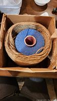 Two large spools of twine and string in a cardboard box from a top view.