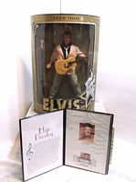 Photo showing Elvis Presley collector doll in original packaging with Teen Idol label and certificate booklet opened showing Elvis Presley biography and stamp details.