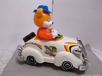 Side view of white police style cartoon car showing bear driver figure wearing a blue cap and orange outfit against plain background.