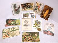 Photo showing 11 antique embossed postcards arranged on a white cloth surface. Postcards feature various designs including children playing, corn cob, flowers, fruits, and holiday scenes.