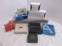 9 different Avon-branded jewelry boxes stacked and arranged, unopened packaging.