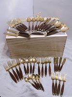 Full set of 45 brass and rosewood utensils displayed on and in front of a wooden box with various forks, spoons, knives, and serving pieces arranged in rows.