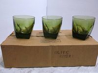 Three avocado green square tumblers displayed on a cardboard box, showing their shape and color.
