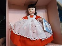 Photo of Madame Alexander Doll #428 Little Nanny Etticoat wearing red dress with white eyelet apron and black hair, holding original tag.