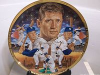 Collector plate showing detailed painted portrait of Mickey Mantle surrounded by smaller images of him playing baseball, gold rim and inscriptions.