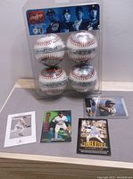 Four Rawlings collector baseballs in original plastic clamshell packaging, showing A-Rod, Jeter, Nomar, and Sosa names, with six assorted baseball trading cards laid out on table below.