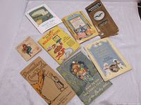 Eight vintage cookbooks and pamphlets arranged on cloth backdrop showing variety of cover art and titles.