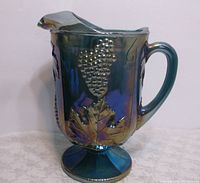 Front angle view of vintage Indiana Harvest Grape iridescent pedestal pitcher with detailed raised grape clusters and leaves.