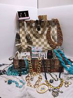 Photo showing a mixed collection of jewelry including necklaces of various bead and chain designs, earrings, bracelets, rings, brooch displayed on and around a chessboard pattern background.