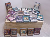 Image showing multiple Yu-Gi-Oh! cards arranged on a wooden crate, some stacked and some spread out. Cards are in protective sleeves with detailed fantasy and monster artwork.