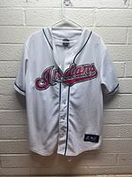 Front view of white Cleveland Indians jersey with red and black script logo. Visible stains and some missing buttons.