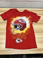 Front view of the red Kansas City Chiefs youth t-shirt with helmet graphic and team logos.