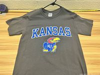 Front view of gray Kansas Jayhawks t-shirt with logo and large text 'KANSAS' across chest.