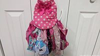 Photo of nine assorted dog clothes hanging on a hook or hanger, including a prominent pink polka dot dress with a large bow.