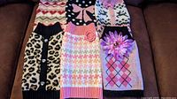 Photo showing six small dog winter sweaters in various patterns and colors arranged on couch