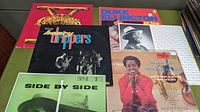 Top view of six vinyl record covers arranged on a green surface showing artist images and titles