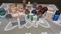 Photo showing a variety of vintage Avon products on a lace tablecloth, including bottles, jars, boxed powders, and creams.
