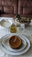 Overview of lot on table showing lidded ceramic duck, plates, glass containers, nut dish, and white scalloped dish