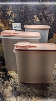 Three large rectangular Tupperware containers with pink lids placed on a countertop.